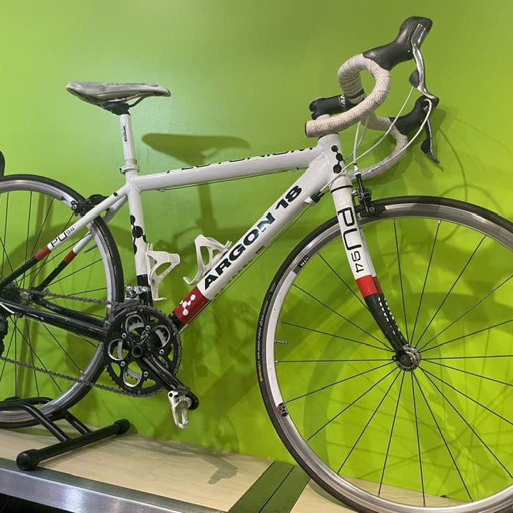 White bicycle with red and black details on a stand against a green wall